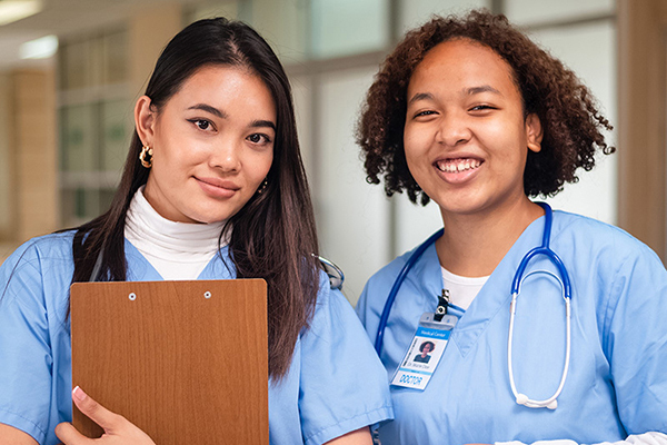 Two young nurses standing by the nurses station smiling