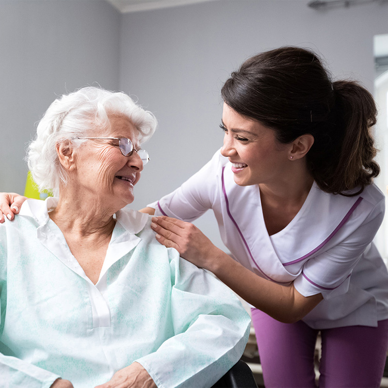 Smiling nurse leaning down to speak with a resident in a wheelchair.